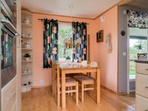 A cozy dining area with a wooden table and chairs, a window with curtains, and a view of greenery outside. - 4 Star Holiday Home in Sparreholm (Sparreholm)