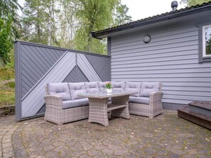 An outdoor seating area with a grey sofa and wicker tables, set against a house with grey siding and a tiled roof. - 4 Star Holiday Home in Sparreholm (Sparreholm)