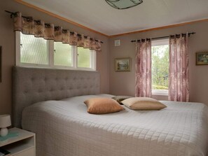 A bedroom with a bed, two pillows, a nightstand, a window with curtains, and a wall-mounted picture. - 4 Star Holiday Home in Sparreholm (Sparreholm)