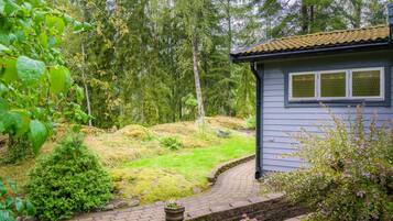 A house with a paved driveway leading to a wooden deck, surrounded by a forested area.
