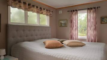 A bedroom with a large bed, a nightstand, a window with curtains, and a wall-mounted picture.