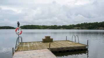 A wooden dock extending into calm water with a lifebuoy attached to a metal railing.
