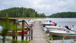 A wooden dock leading to a row of boats docked at a calm lake, surrounded by dense forest. - 4 Star Holiday Home in Sparreholm (Sparreholm)