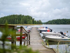 A wooden dock leading to a row of boats docked at a calm lake, surrounded by dense forest. - 4 Star Holiday Home in Sparreholm (Sparreholm)