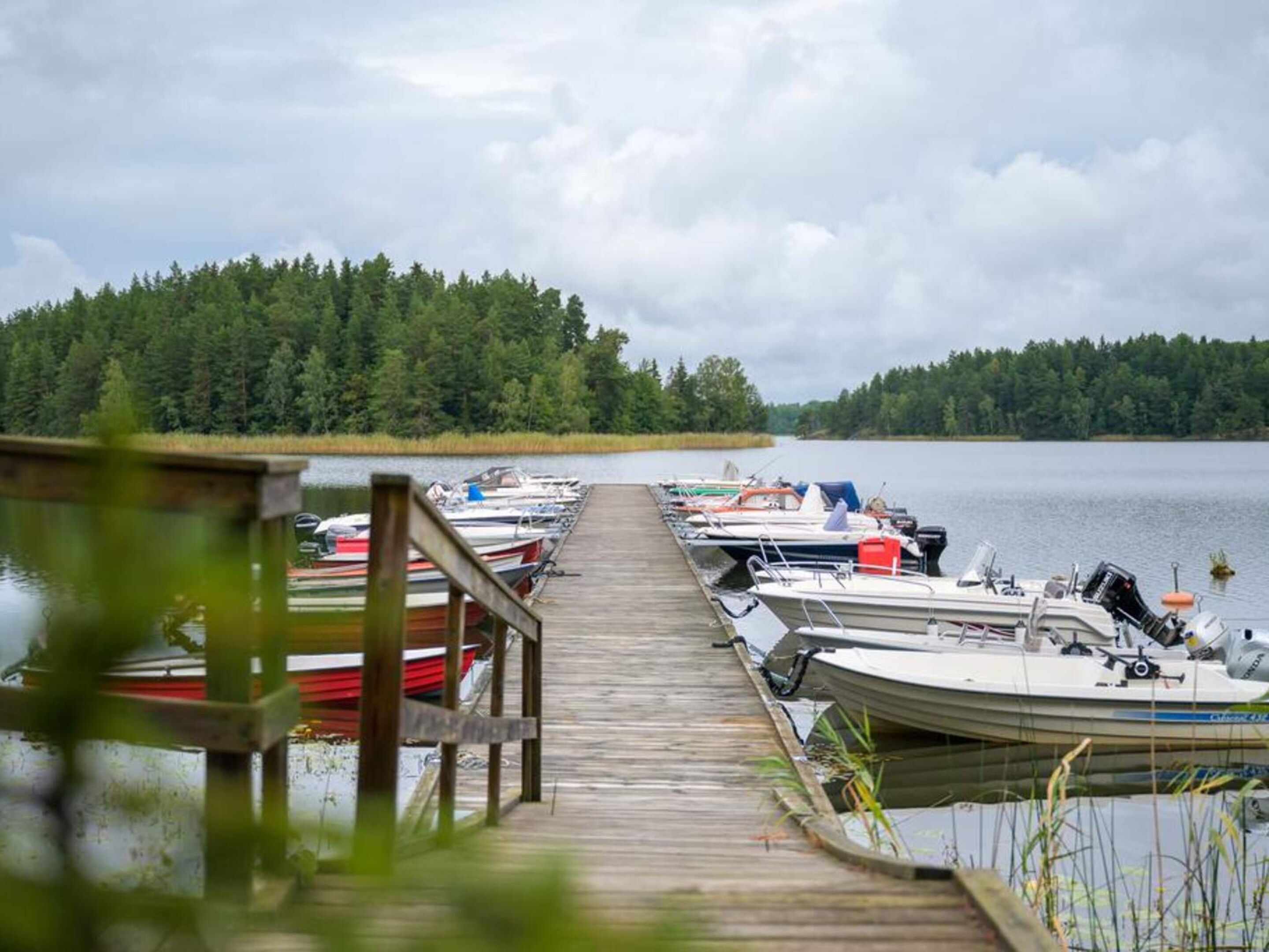 A wooden dock leading to a row of boats docked at a calm lake, surrounded by dense forest.
