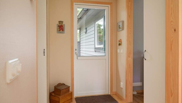 Una puerta de madera con un pequeño escalón que conduce al umbral, un felpudo y un interruptor de luz en la pared.