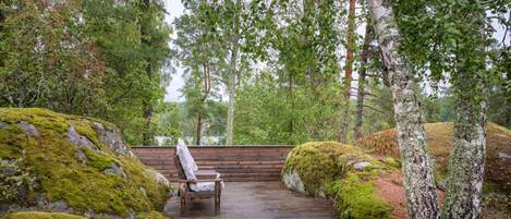 A wooden deck with a bench, surrounded by moss-covered rocks and birch trees.