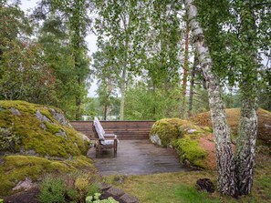 Una terraza de madera con un banco, rodeada de rocas cubiertas de musgo y árboles de abedul.