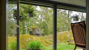Una terraza de madera con una silla, un jardín de rocas y vista a un bosque a través de amplios ventanales.