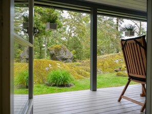 A wooden deck with a chair, a rock garden, and a view of a forest through large glass doors. - 4 Star Holiday Home in Sparreholm (Sparreholm)