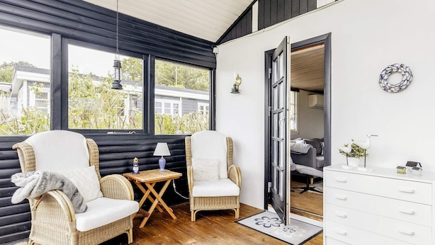 Een gezellige kamer met rieten stoelen, een klein tafeltje met een lamp en een witte ladenkast.
