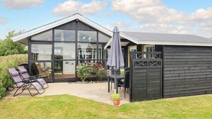 Een modern huis met een groot raam, een terras met stoelen en een tuin.