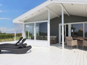 En overdækket terrasse med siddeplads, et bord og en liggestol.