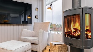 Ein gemütliches Wohnzimmer mit einer Couch, einem kleinen Hocker, einem Kamin und einem Fernseher an der Wand.