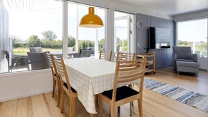 Ein Essbereich mit Tisch, Stühlen, großen Fenstern, einem Fernseher und einer Couch.