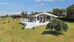 Ein modernes Haus mit überdachter Terrasse, Rasenfläche und einem großen Baum.