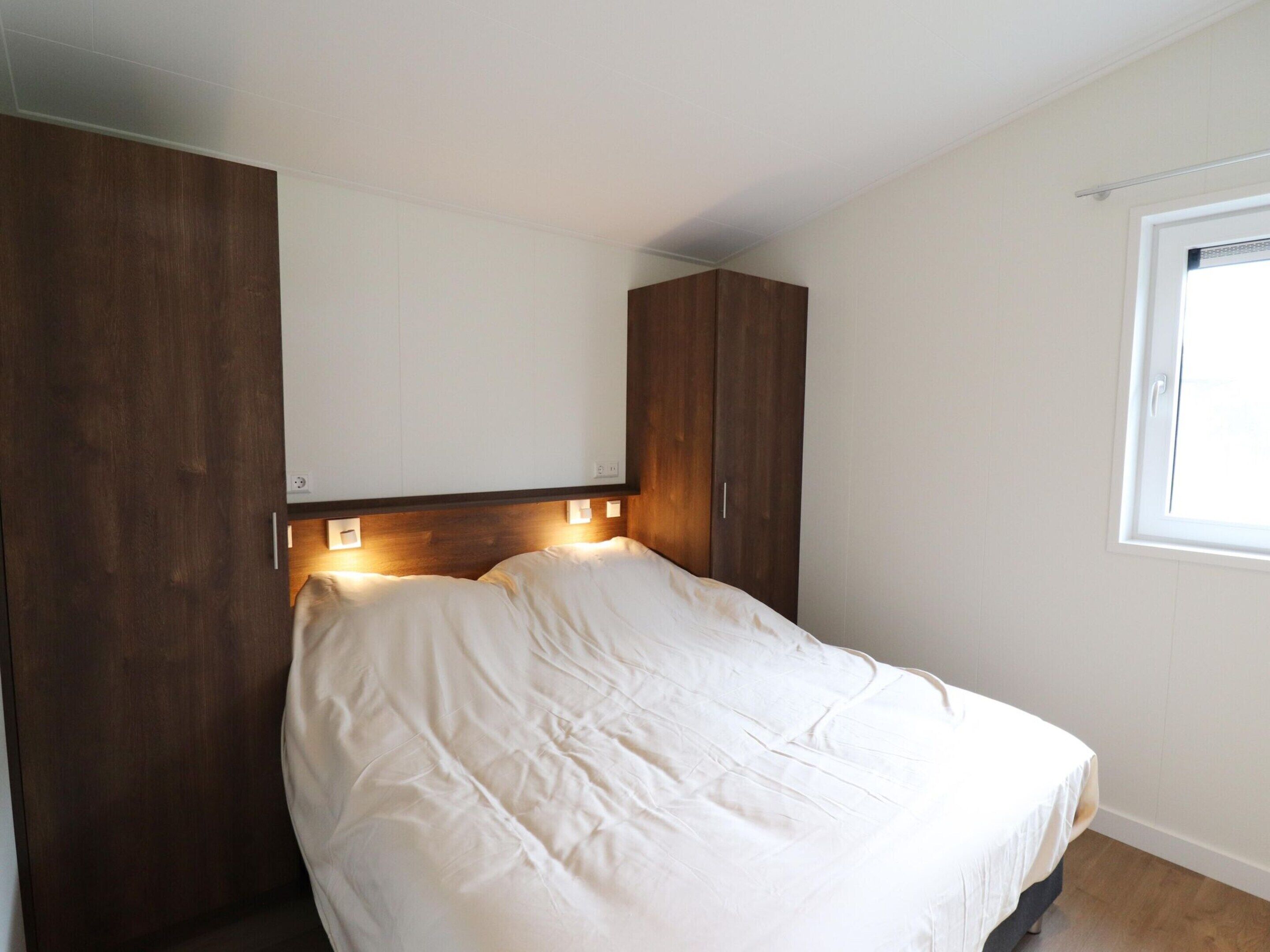 A bedroom with a bed, wooden wardrobe, and a window.