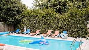 Une piscine avec des jeux gonflables, des chaises longues et une clôture en bois en arrière-plan.