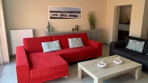 A living room with a red sectional sofa, a black sofa, a wooden coffee table, and a radiator. - Canal-side Family Retreat (Nieuwpoort)