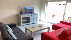 A living room with a grey sofa, a red sofa, a wooden coffee table, and a TV on a white cabinet. - Canal-side Family Retreat (Nieuwpoort)