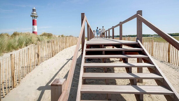 A wooden boardwalk leading to a lighthouse, with a sandy beach and grassy dunes on either side. - Canal-side Family Retreat (Nieuwpoort)