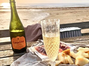 A bottle of Campo Viejo Cava, a glass of champagne, and a platter of cheese on a wooden table by the beach. - 9 Person Holiday Home in Skummeslovsstrand (Skummesloevsstrand)