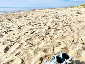 A pair of sneakers on a sandy beach with footprints, a clear sky, and a calm sea in the background. - 9 Person Holiday Home in Skummeslovsstrand (Skummesloevsstrand)