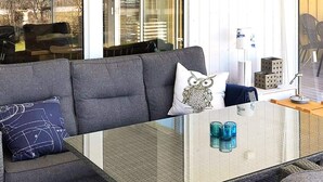 Een moderne woonkamer met een grijze bank, een glazen salontafel en decoratieve kussens.