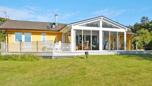 Een modern huis met een grote glazen conservatorium, een omheind terras en een verzorgd gazon.