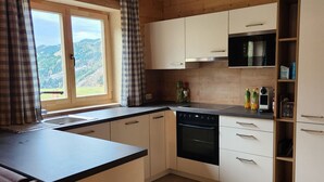 A kitchen with a view of a mountainous landscape through a window, wooden cabinets, a black countertop, and a dishwasher. - Alpine hut in Rauris ski Hiking Area With Sauna (Rauris)