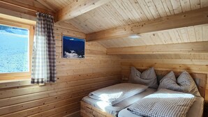 A wooden cabin room with a bed, a window with curtains, and a framed picture on the wall. - Alpine hut in Rauris ski Hiking Area With Sauna (Rauris)
