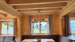 A wooden cabin interior with a dining area, two sofas, and large windows with curtains. - Alpine hut in Rauris ski Hiking Area With Sauna (Rauris)