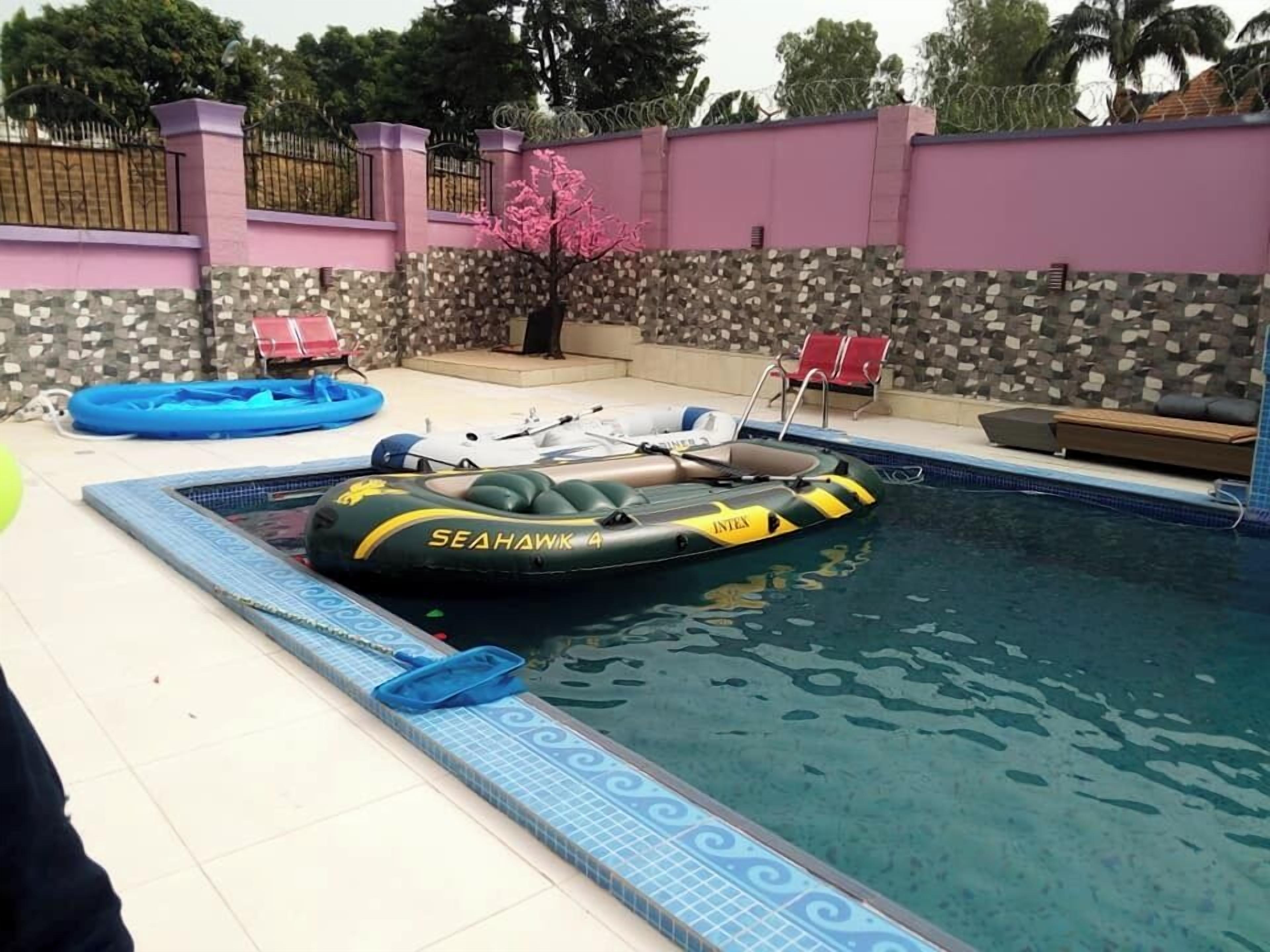Uma piscina com uma bóia inflável Sea Hawk 4, um deck ladrilhado e um muro de pedra com cerca rosa.