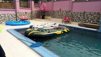Uma piscina com uma bóia inflável Sea Hawk 4, um deck ladrilhado e um muro de pedra com cerca rosa.