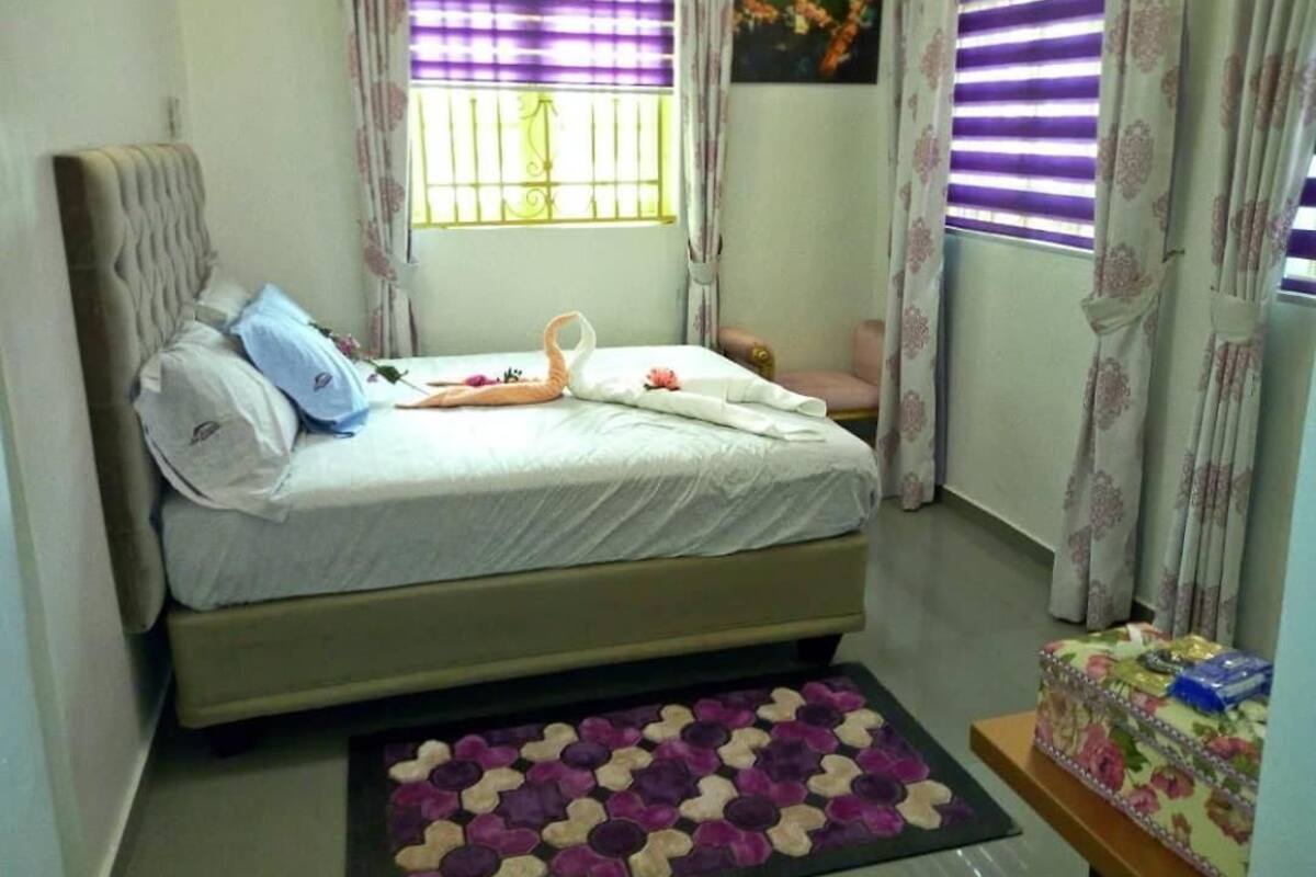 A bedroom with a bed, a bedside table, a window with curtains, and a floral-patterned rug.