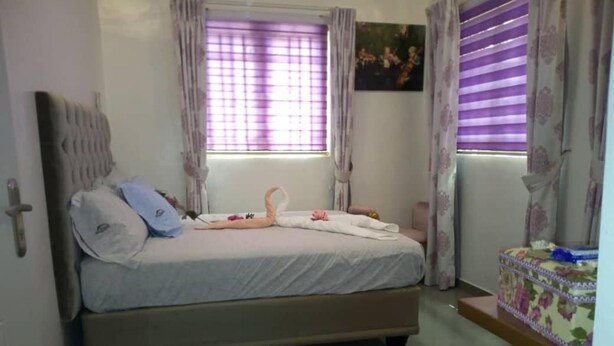A bedroom with a bed, a small table, and a window with curtains. - Lavender Spa and Suites (Enugu)
