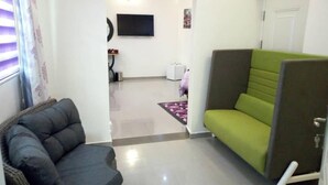 A room with a dark grey sofa, a green sofa, a flat-screen TV mounted on the wall, and a door with a handle. - Lavender Spa and Suites (Enugu)