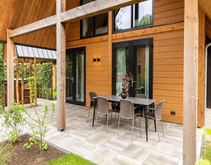 A wooden house with a covered patio, a table with chairs, and a garden area. - Forest Villa 6 Persons (Wekerom)