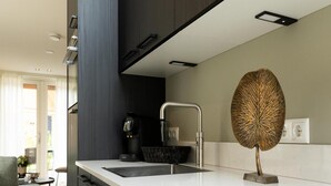 Eine moderne Küche mit weißer Arbeitsplatte, einer Kaffeemaschine und einer dekorativen Blattform-Skulptur.