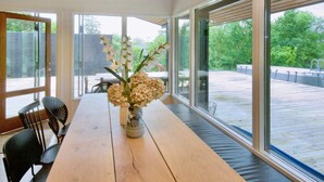 A dining area with a wooden table, chairs, and a vase with flowers. Large windows provide views of the outdoors. - 4 Star Holiday Home in Vejby (Vejby)