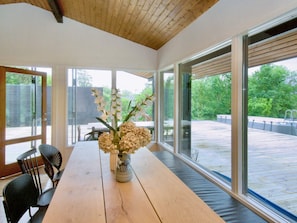 A dining area with a wooden table, chairs, and a vase with flowers. Large windows provide views of the outdoors. - 4 Star Holiday Home in Vejby (Vejby)
