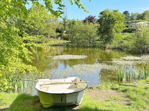 A small boat tied to a grassy bank by a calm pond surrounded by lush greenery and trees. - 4 Star Holiday Home in Vejby (Vejby)