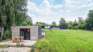 A modern house with a wooden exterior, a patio with a table and chairs, and a large grassy yard. - 4 Star Holiday Home in Vejby (Vejby)
