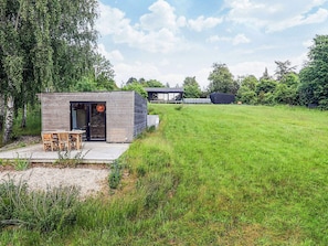A modern house with a wooden exterior, a patio with a table and chairs, and a large grassy yard. - 4 Star Holiday Home in Vejby (Vejby)