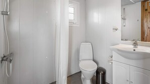A bathroom with a shower, toilet, sink, and a trash bin.