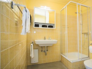 A bathroom with yellow tiles, a white sink, a glass-enclosed shower, and a mirror above the sink.