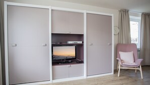 Ein Zimmer mit Schiebetürenschrank, Fernseher auf einem Schrank und einem rosa Sessel, außerdem Holzboden.