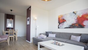 A modern living room with a grey sofa, a white coffee table, and a dining area with a wooden table and chairs. - Gemutliches Apartment in Winterberg mit Balkon (Winterberg)
