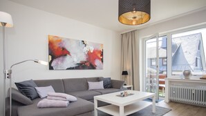 A modern living room with a grey sofa, a white coffee table, and a large abstract painting on the wall. - Gemutliches Apartment in Winterberg mit Balkon (Winterberg)