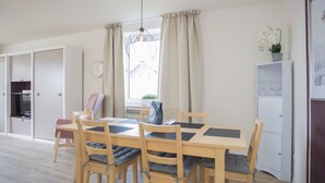 A dining area with a wooden table and chairs, a hanging light fixture, and a view of the outside through a window with curtains. - Gemutliches Apartment in Winterberg mit Balkon (Winterberg)